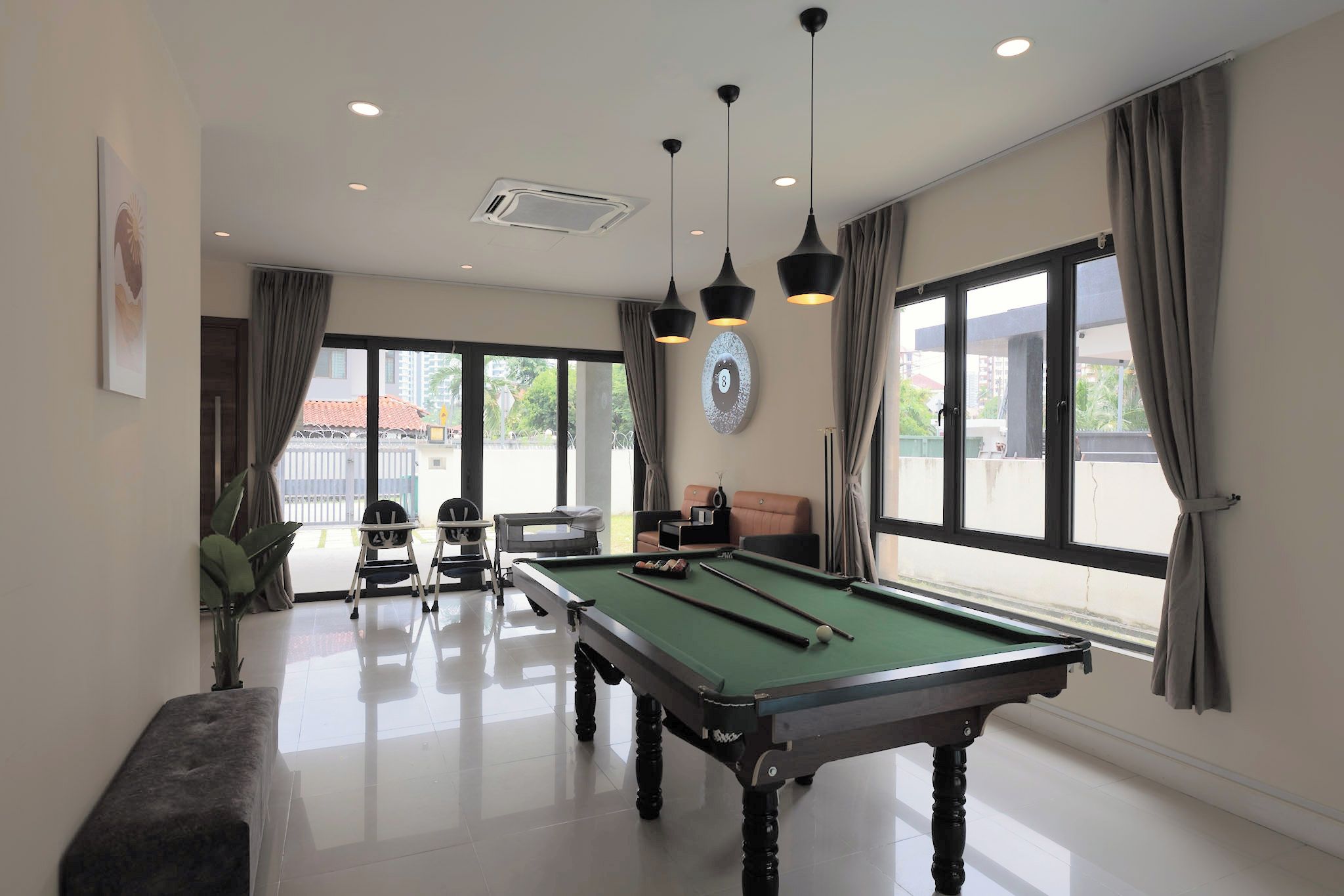 A pool table in a room with large windows, a sofa, and a dining table.