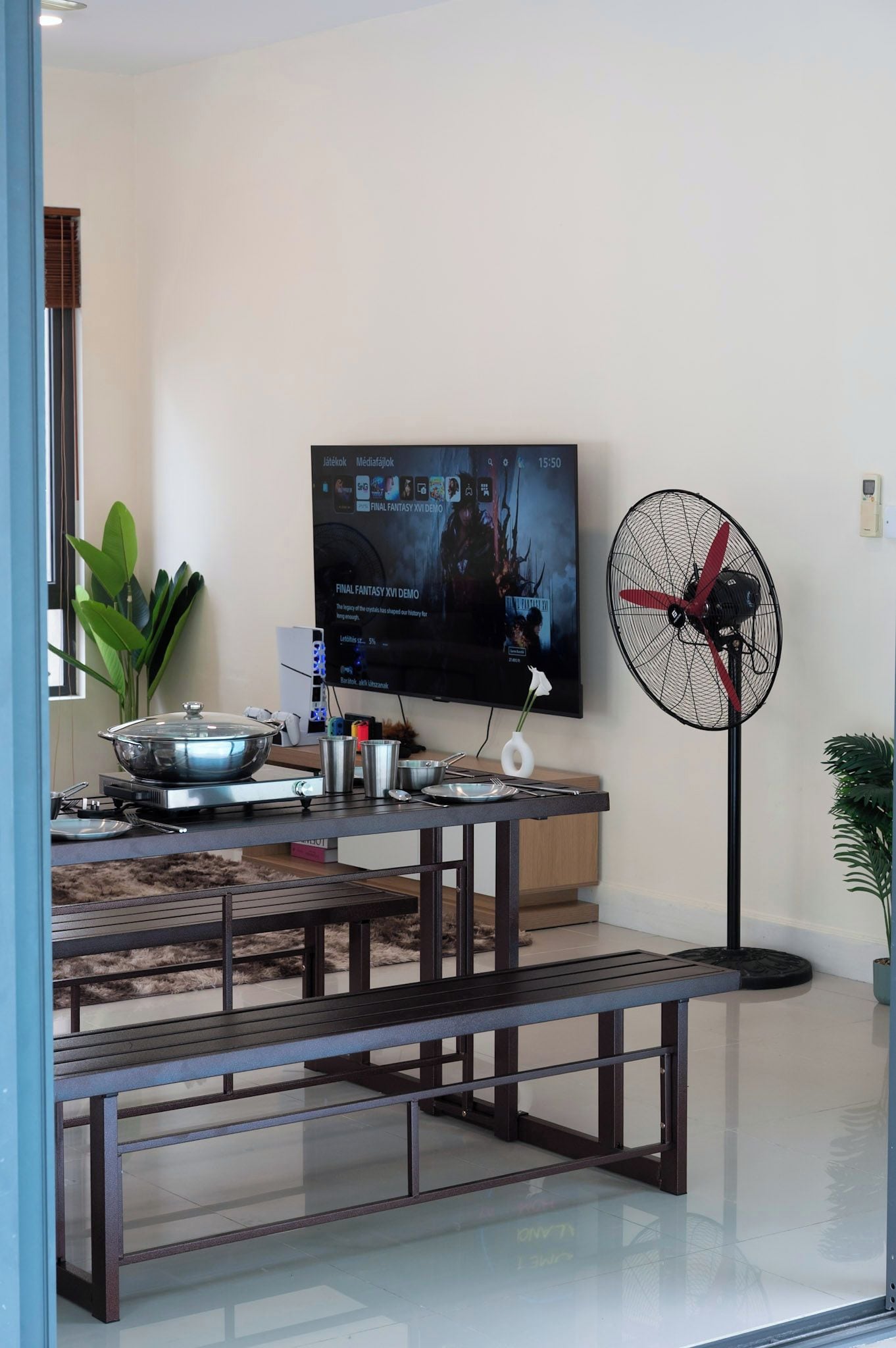 A modern living room with a flat-screen TV, a standing fan, and a dining area with a bench.