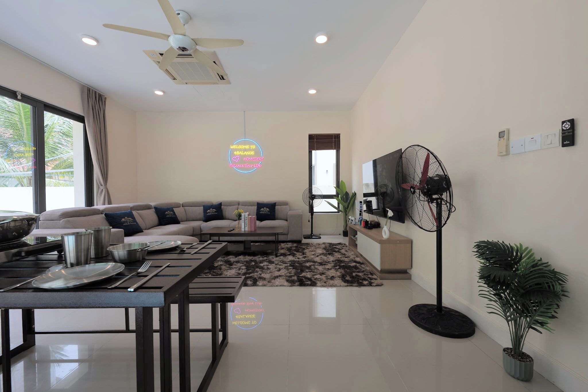 A modern living room with a sofa, dining table, ceiling fan, and a TV mounted on the wall.