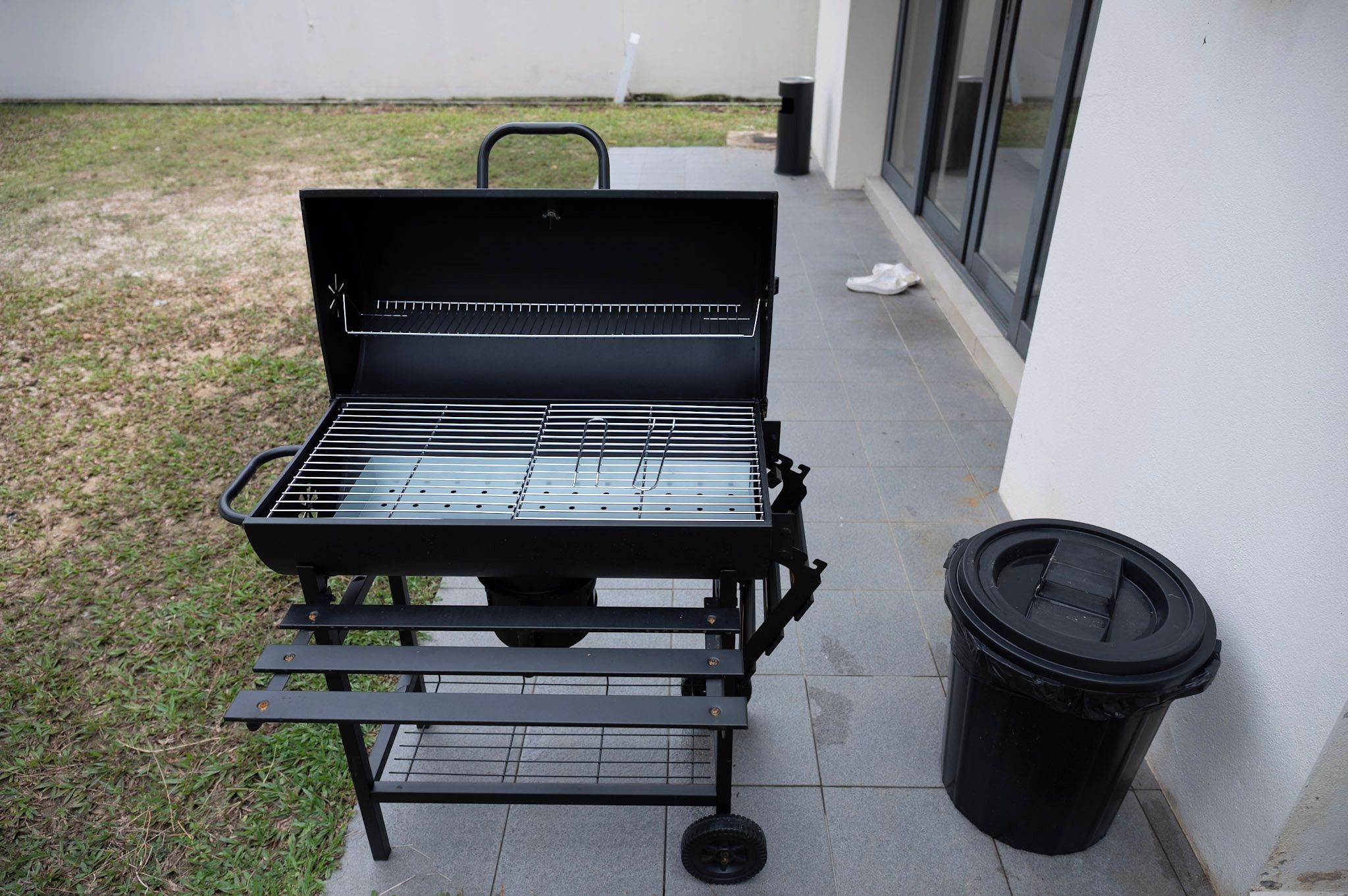 A black barbecue grill with a metal grate, a small table, and a trash can.