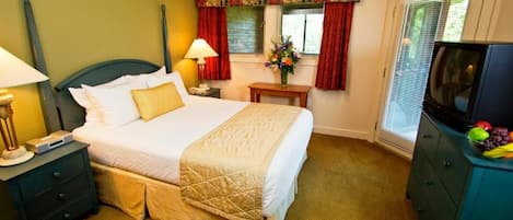 Habitación de hotel con cama, mesita de noche, lámpara, televisión y ventana con cortinas.