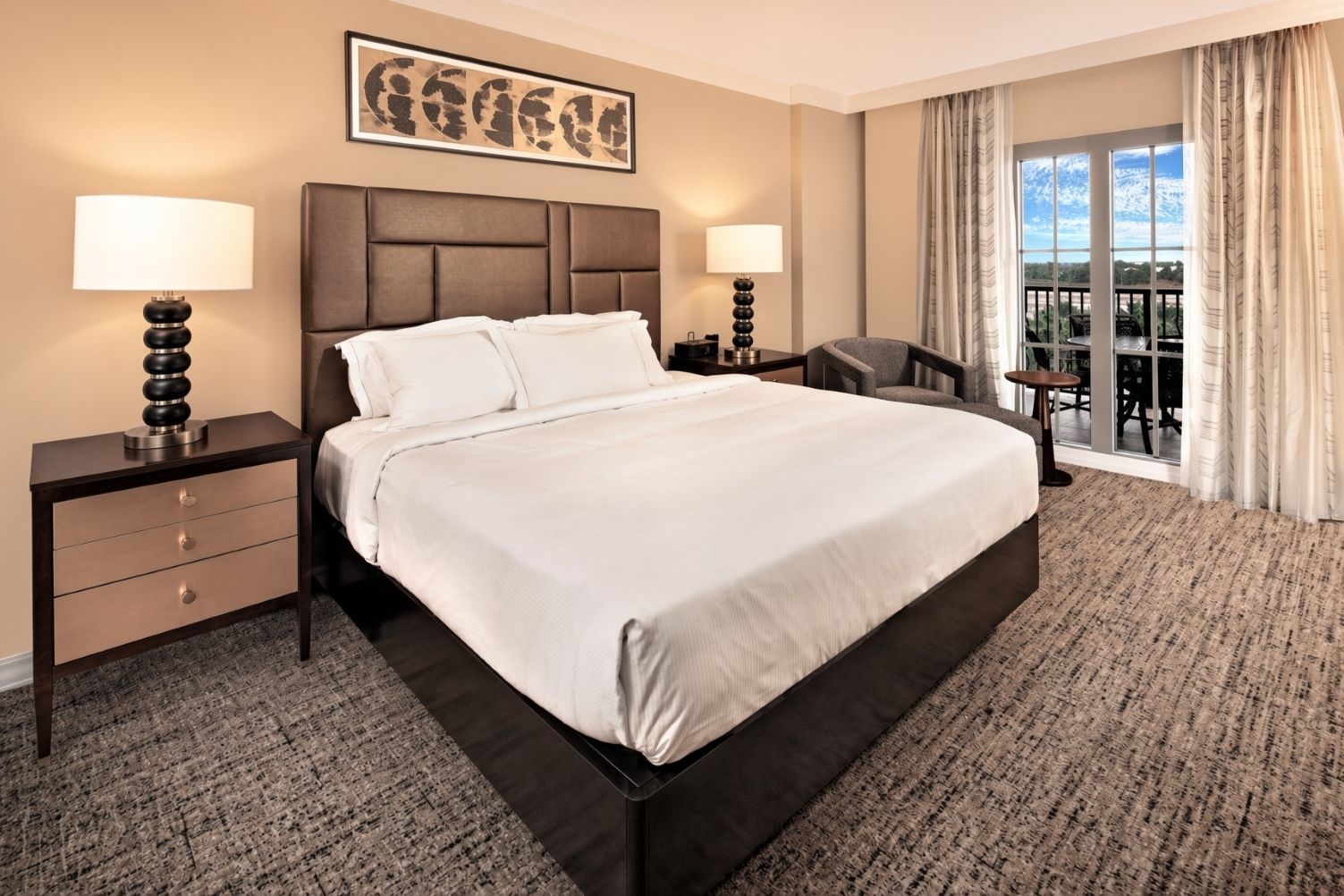 A hotel room with a large bed, two bedside tables with lamps, a chair, a desk, and a view of the outdoors.