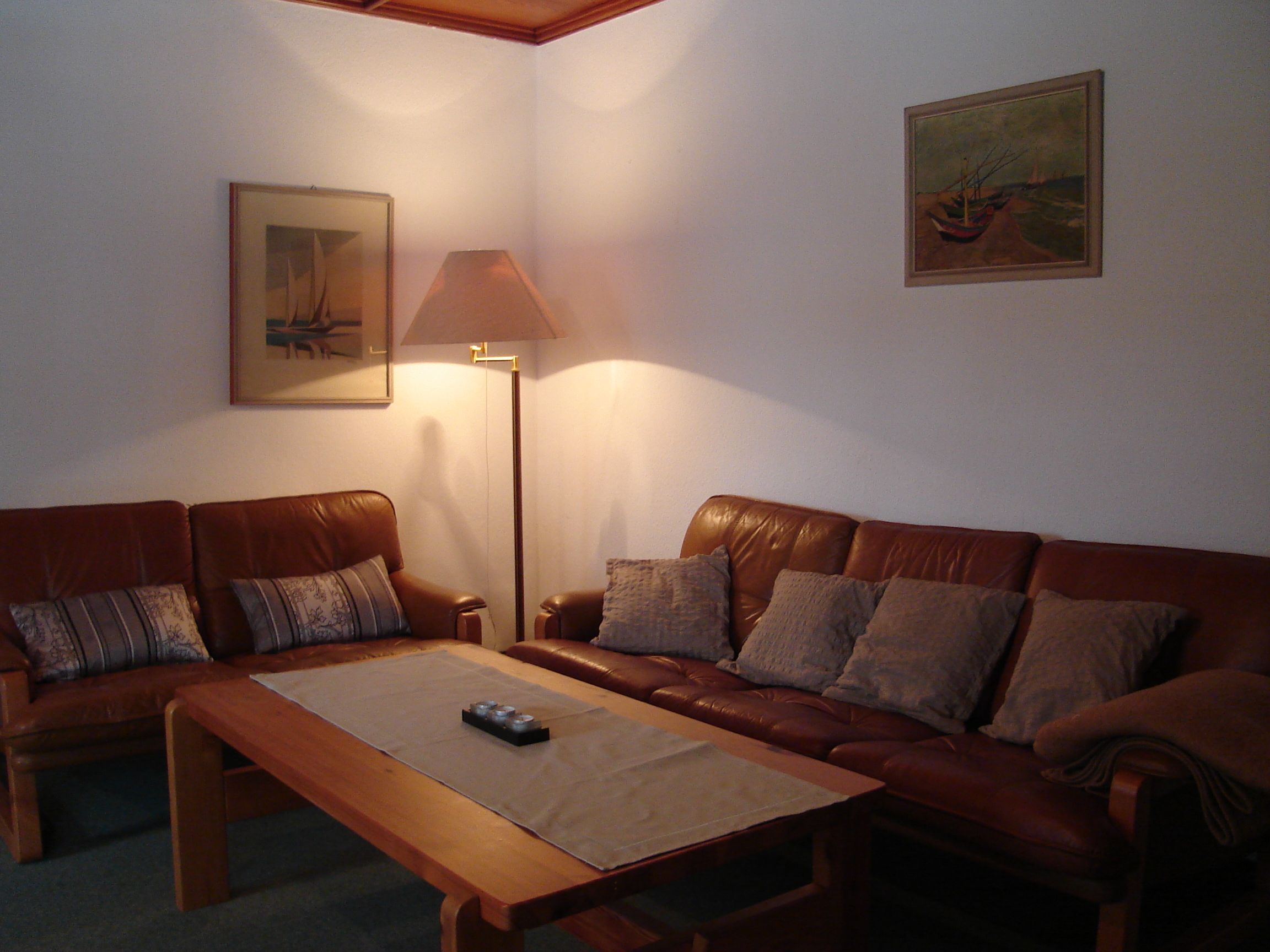 Uma sala de estar com um sofá de couro marrom, uma mesa de centro de madeira, um abajur e duas obras de arte emolduradas nas paredes.