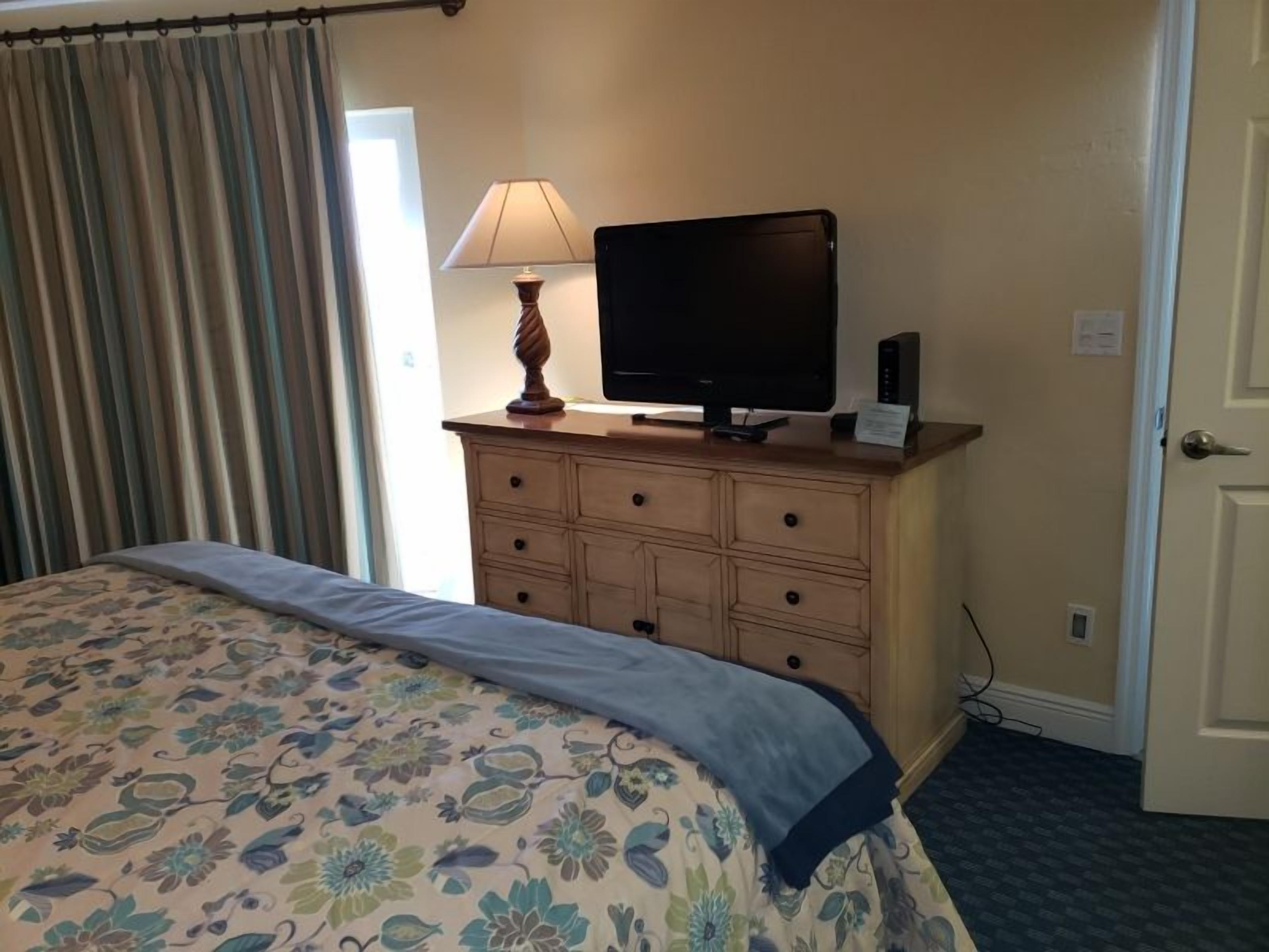 Een hotelkamer met een bed, een televisie op een dressoir en een deur.