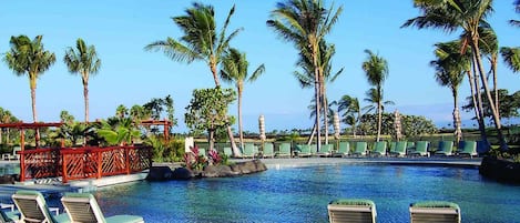 A pool area with lounge chairs, palm trees, and a clear sky.