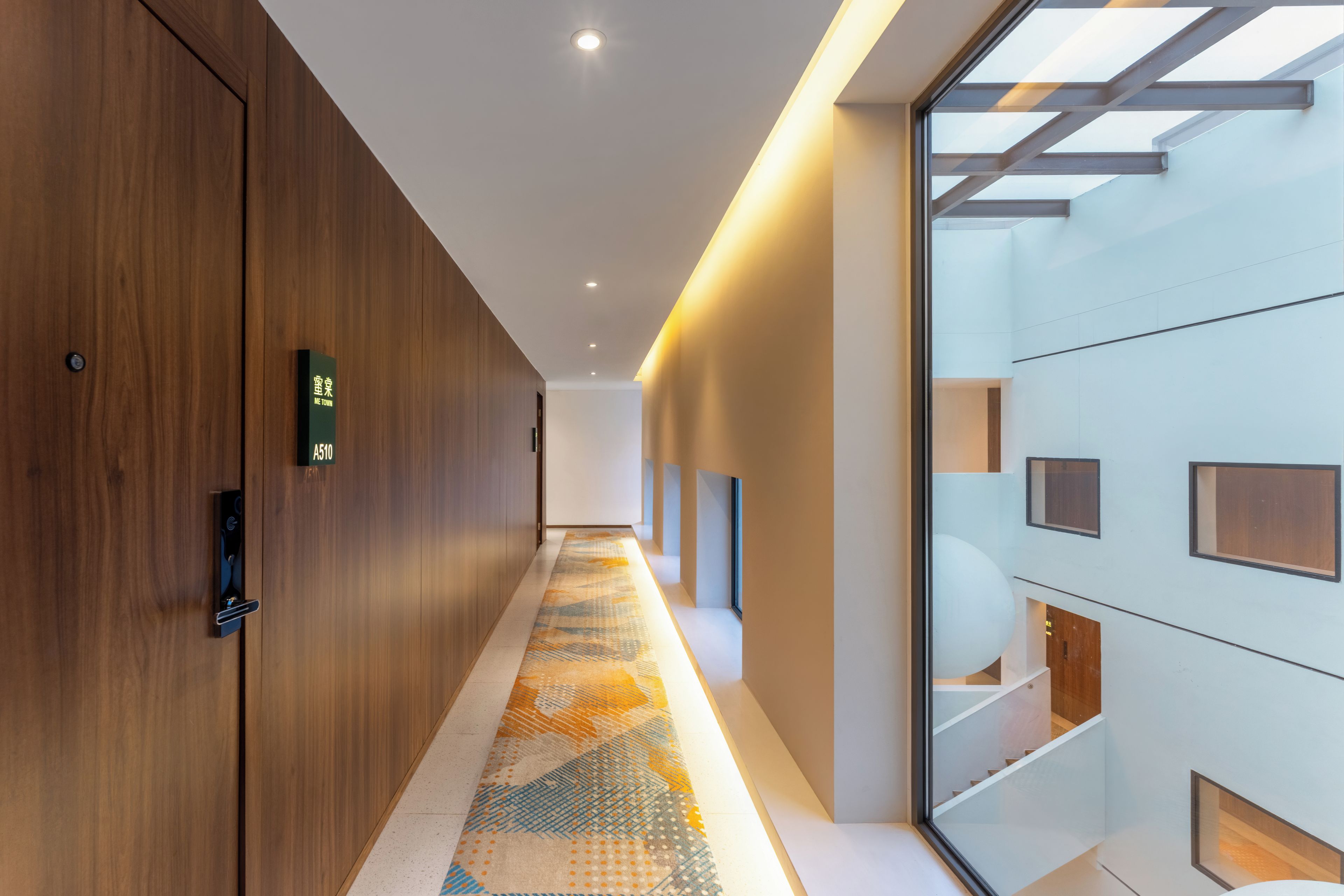 A modern hallway with a wooden wall, a patterned carpet, and a glass partition with built-in lighting.