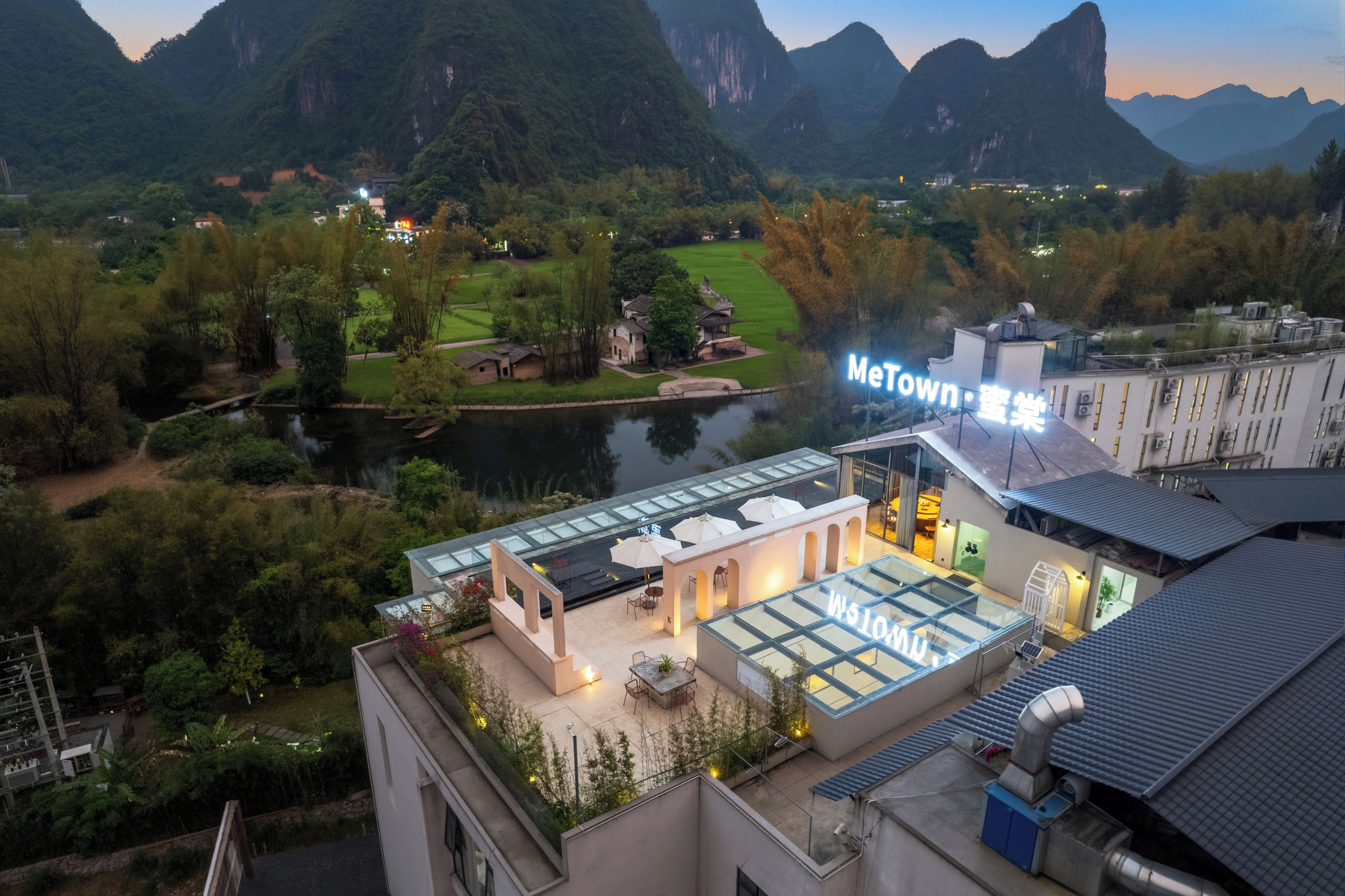 A hotel with a rooftop terrace, a view of the surrounding mountains, and a sign that reads 'MeTown'.