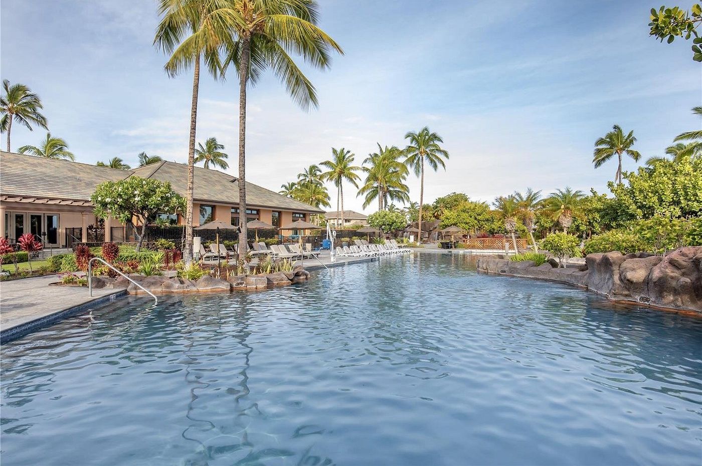 A swimming pool with lounge chairs, palm trees, and a building with a tiled roof.