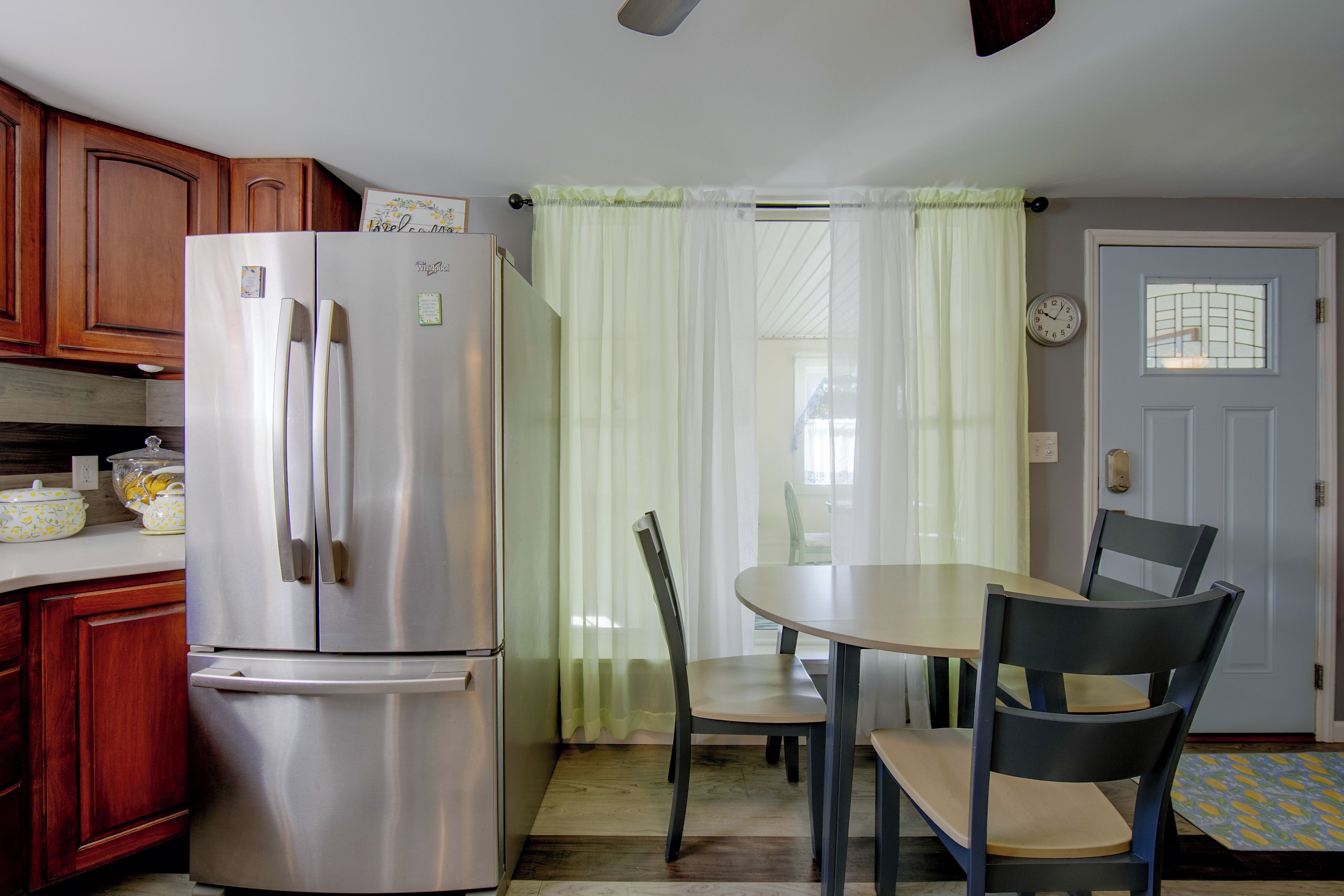 A kitchen with a stainless steel refrigerator, wooden cabinets, a dining table with chairs, and a door with a window.
