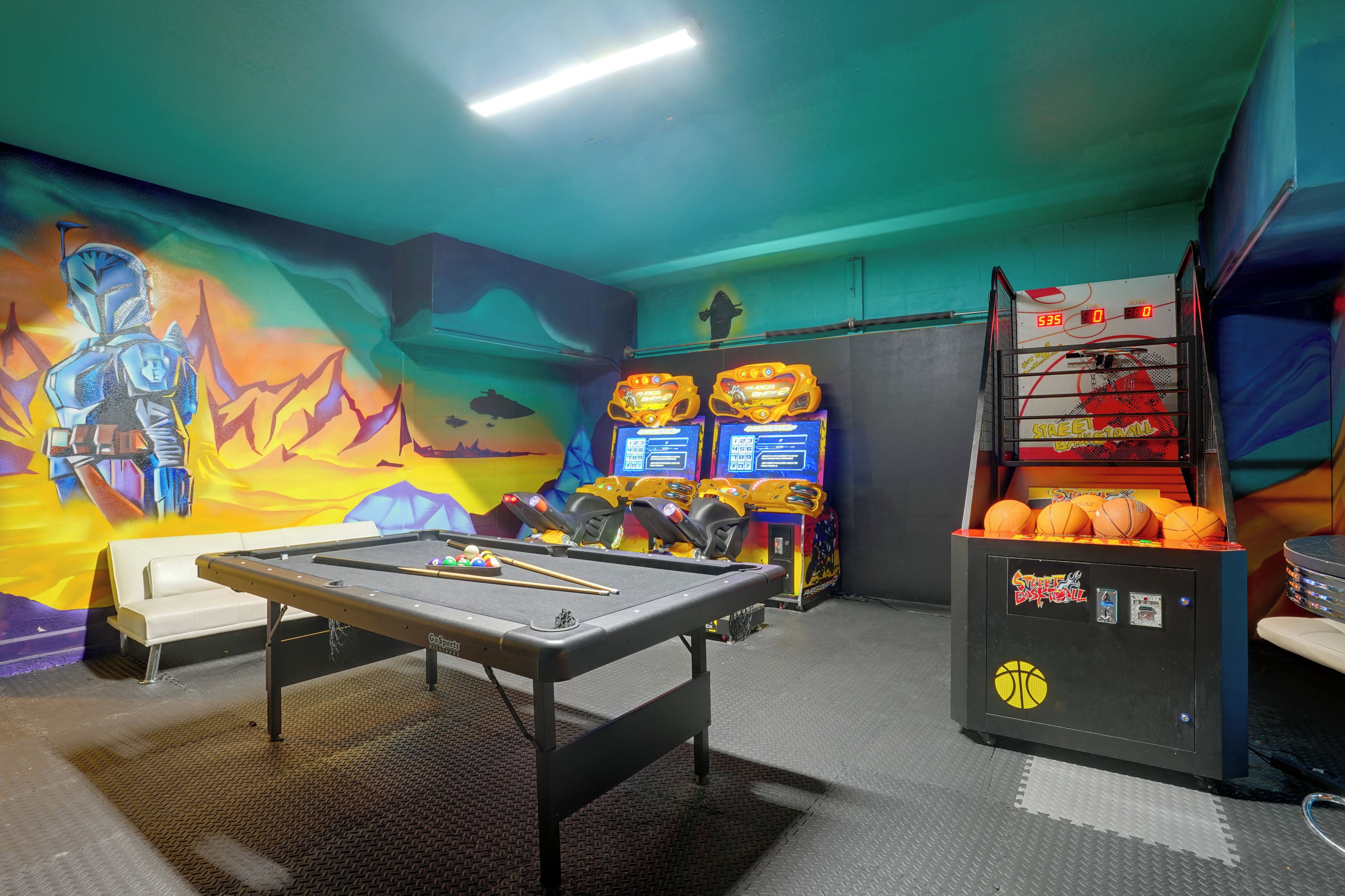 A pool table with billiard balls, a mural, and arcade machines in a recreational area.