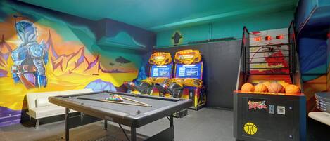A pool table with billiard balls, a mural, and arcade machines in a recreational area.