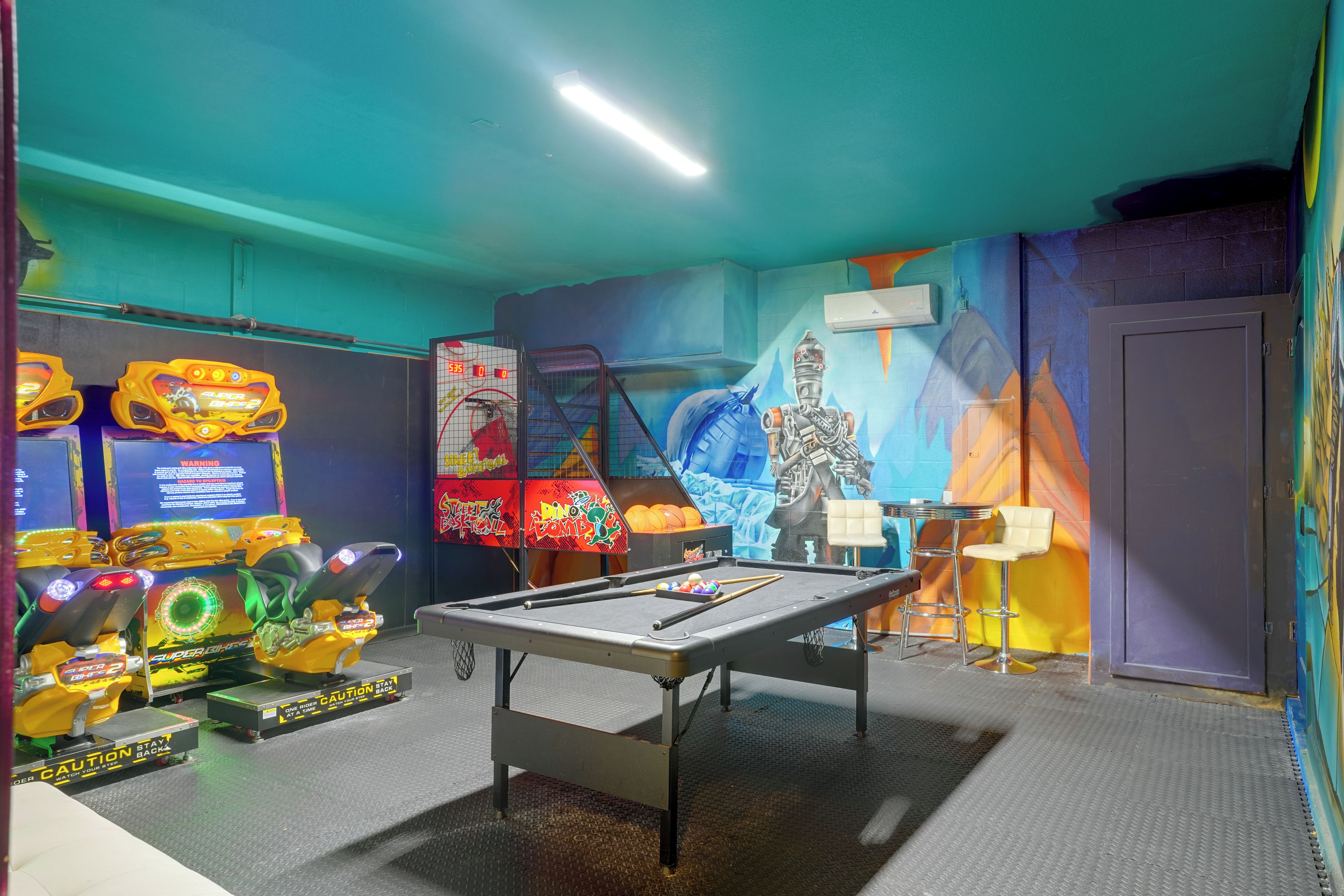 A room with a pool table, arcade games, and a mural.