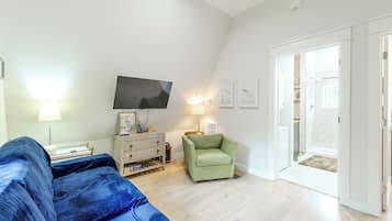 A modern living room with a flat-screen TV, a green armchair, a sofa, and a wooden cabinet.