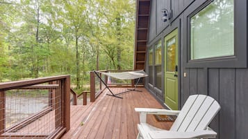 Una terrazza in legno con un'amaca, una sedia bianca e una porta con una finestra.