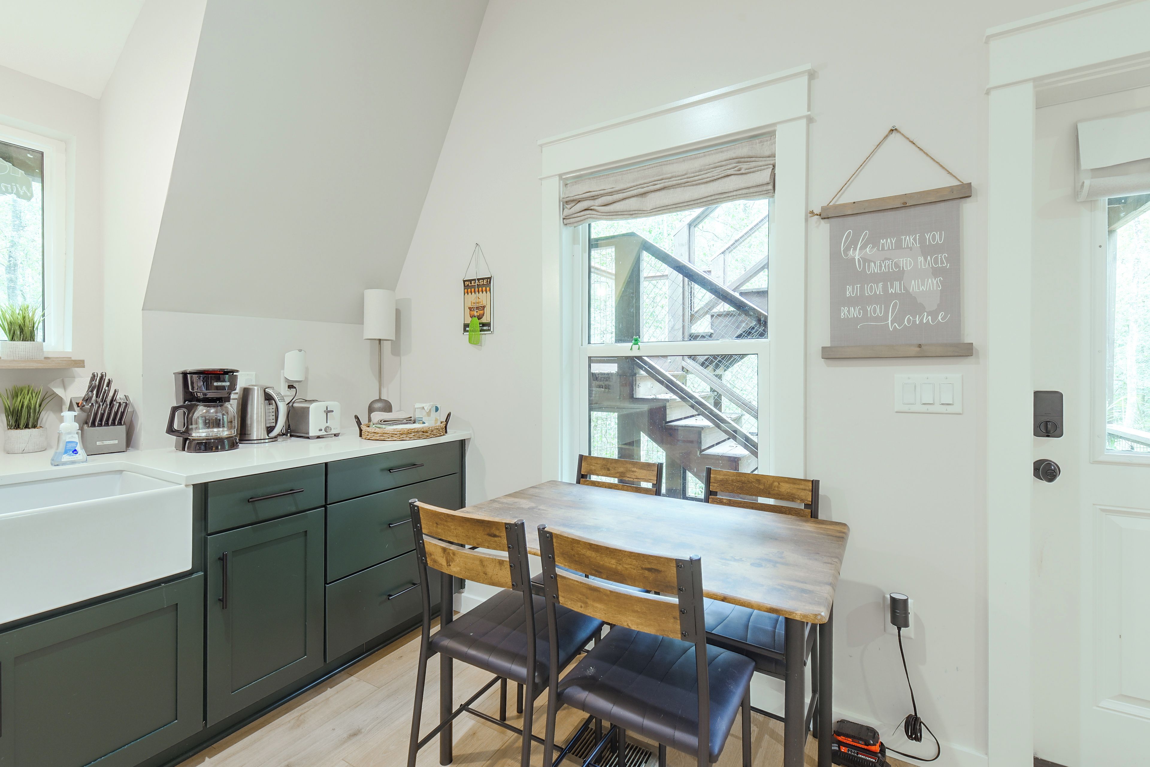 Una cucina moderna con zona pranzo, caratterizzata da una scala che conduce a un livello superiore, una macchina da caffè e vista sull'esterno.