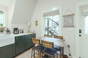 A modern kitchen with a dining area, featuring a staircase leading to an upper level, a coffee machine, and a view of the outside. - Walk to Choctawhatchee River! A-Frame Cabin Escape (Ponce de Leon)