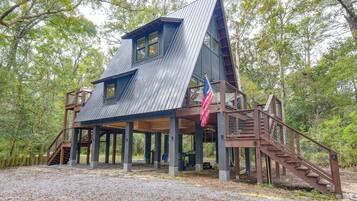 Una baita a più livelli con tetto in metallo, veranda in legno e un'asta sventolante.