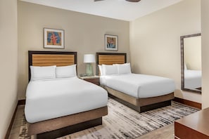 Quarto de hotel com duas camas, um espelho, obras de arte nas paredes e um tapete estampado.