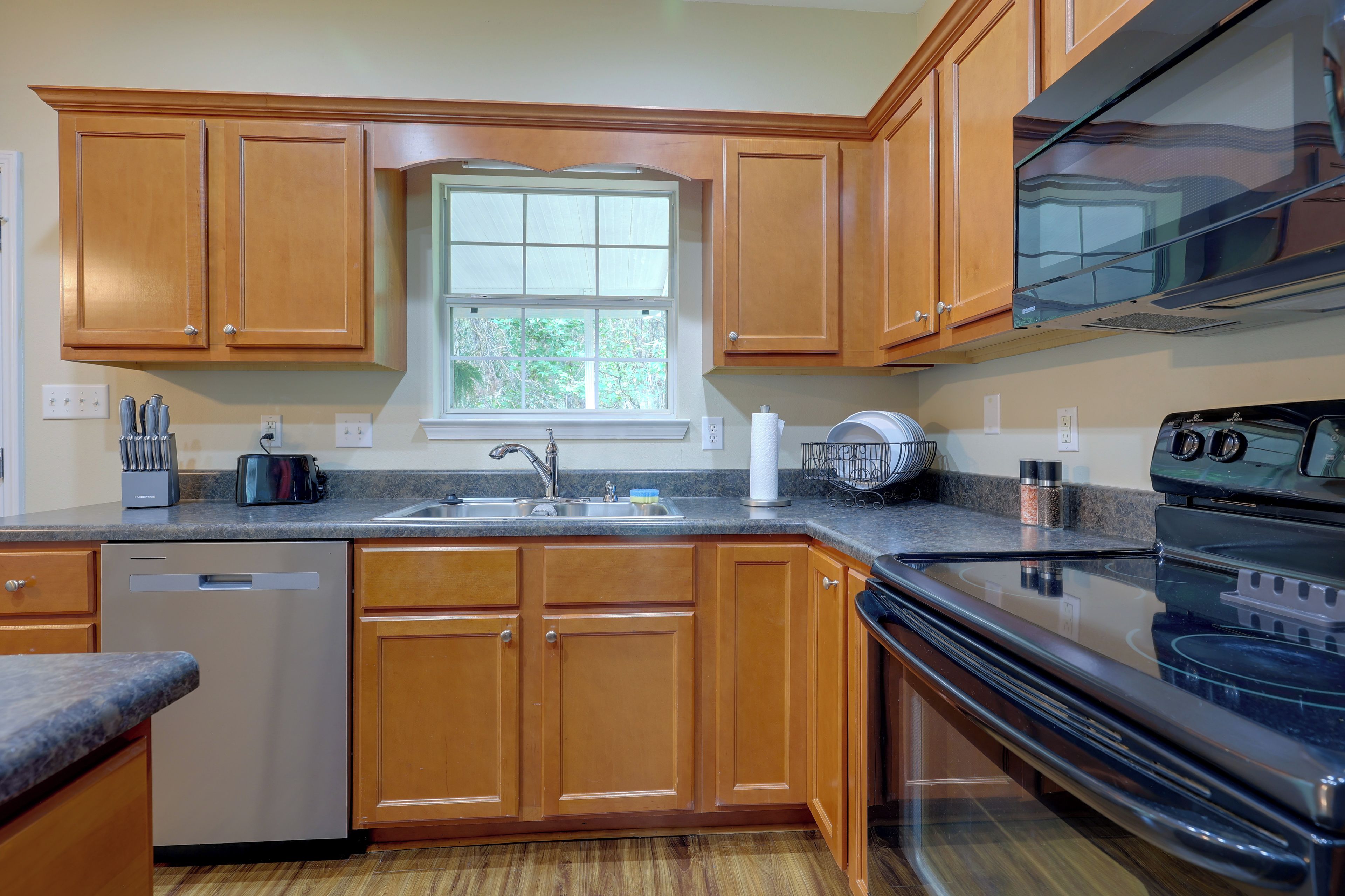 A kitchen with wooden cabinets, a stainless steel sink, a dishwasher, and a black stove.