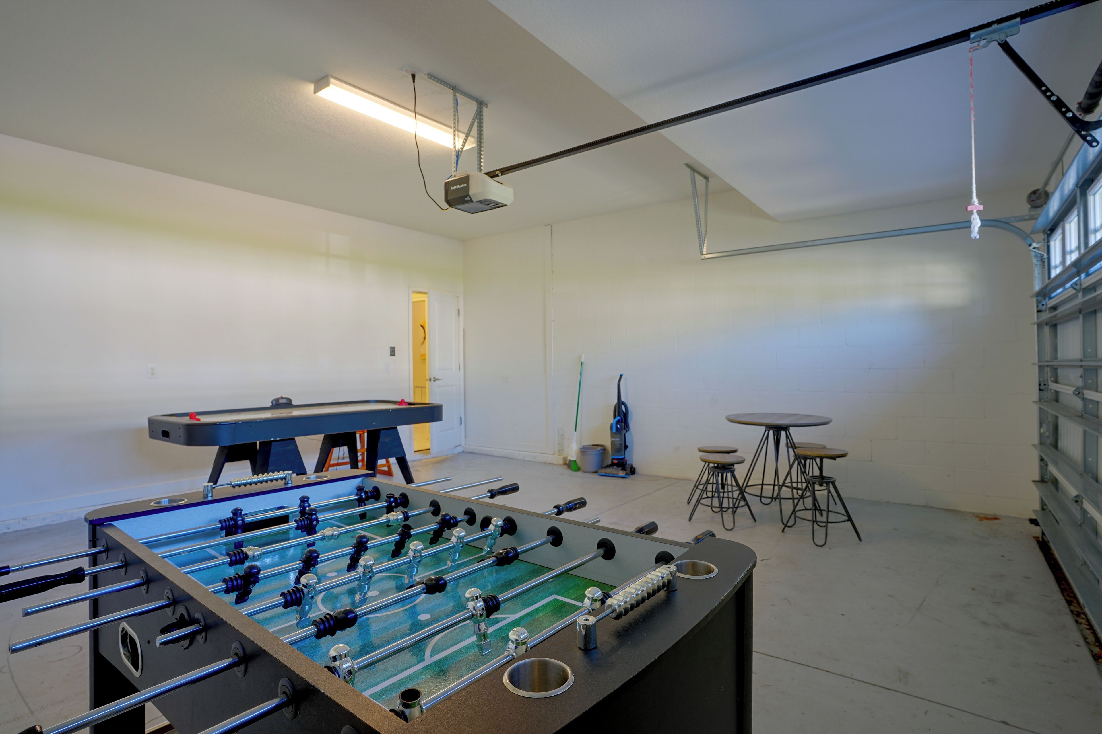 A room with a foosball table, a small table with stools, and a ceiling-mounted projector.