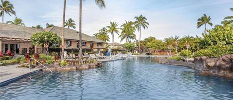 A swimming pool with lounge chairs, palm trees, and a building with a tiled roof.