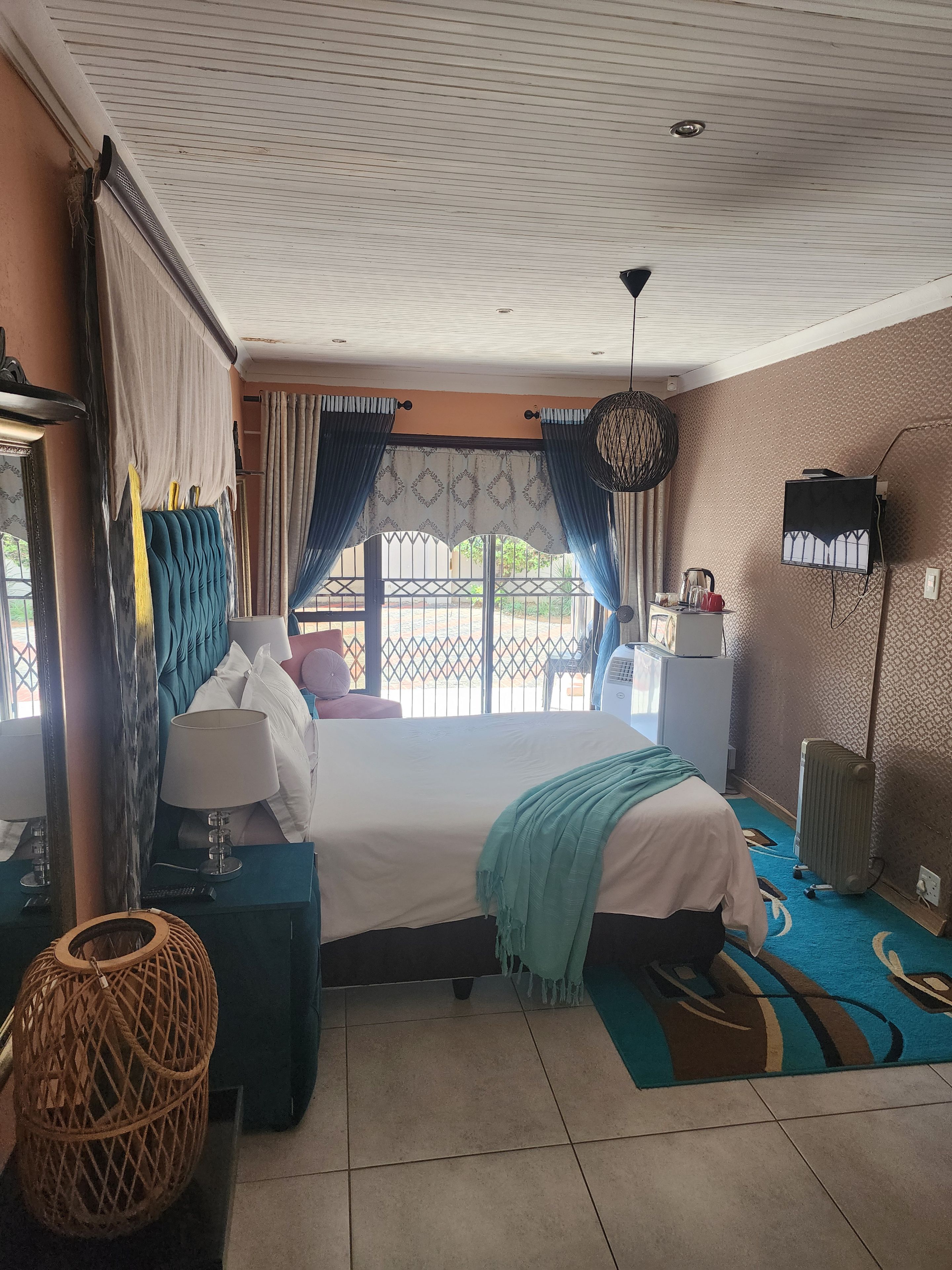 A hotel room with a bed, a desk, a chair, a lamp, a hanging light fixture, and a view of the outdoors.