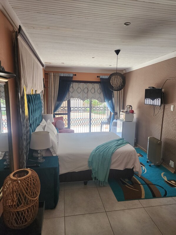 Quarto de hotel com cama, escrivaninha, cadeira, abajur, luminária pendente e vista para o exterior.