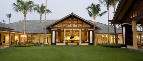 A modern resort with a covered outdoor area, palm trees, and a well-maintained lawn.