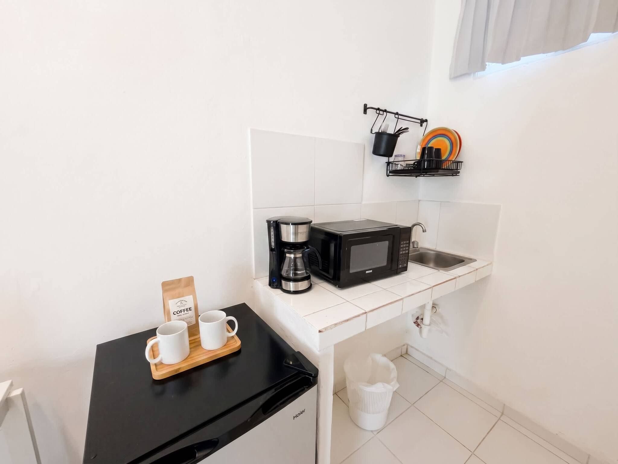 Una kitchenette compacta con cafetera, microondas y un lavamanos pequeño.
