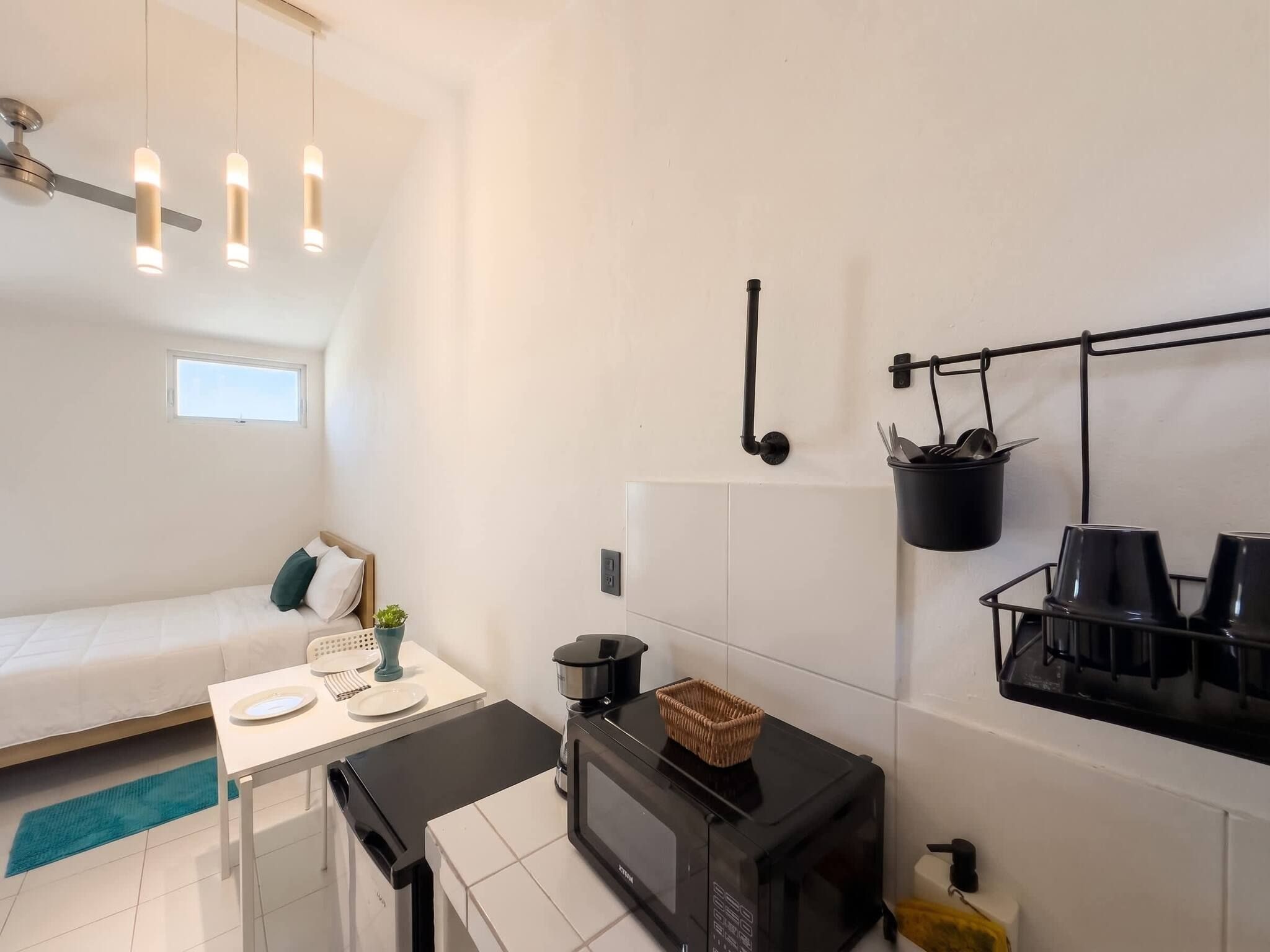 A compact kitchenette with a microwave, a small dining table, and a bed in the adjacent room.