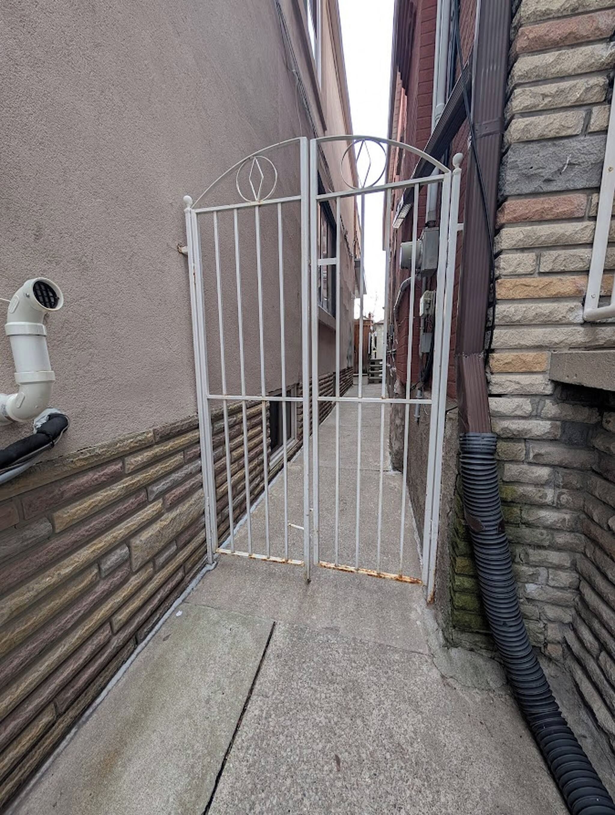 A gated alleyway with a metal gate, a concrete path, and a building with stone and brick walls.
