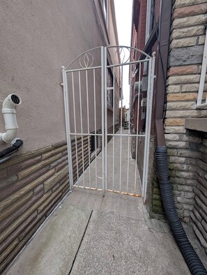 Un passatge tancat per una reixa de metall, un camí de formigó i un edifici amb parets de pedra i maó.