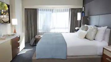 A hotel room with a large bed, a desk with a lamp, a television, and a window with curtains.