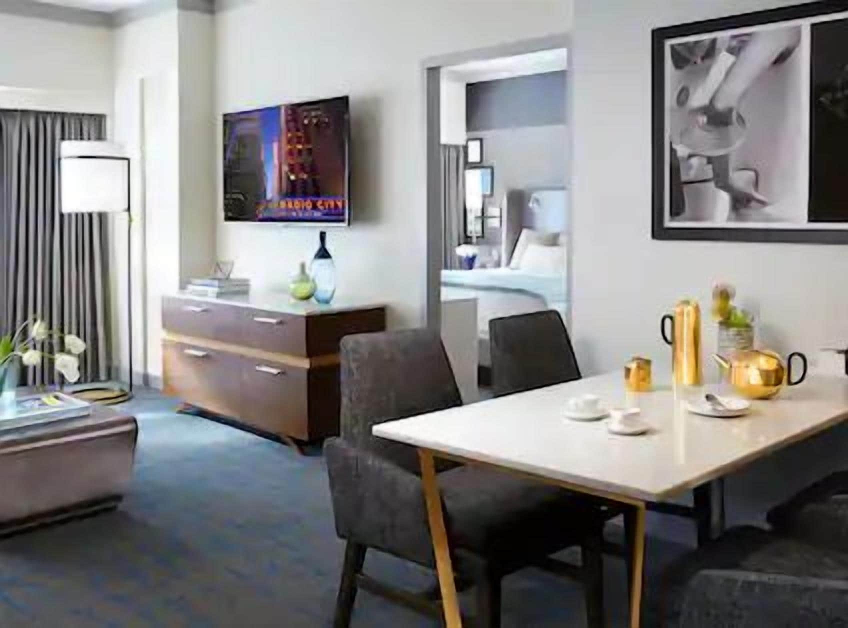 A hotel room with a bed, a desk with a chair, a TV, and a framed picture on the wall.