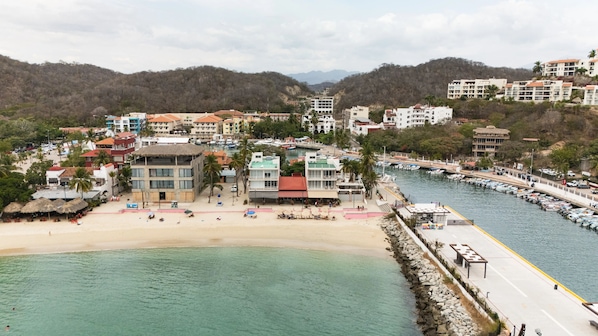 Un pueblo costero con playa, puerto deportivo y edificios con balcones que dan al agua.