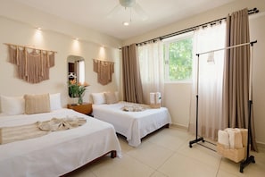 Habitación de hotel con dos camas, un ventanal grande con cortinas, un ventilador de techo y un espejo fijado a la pared.