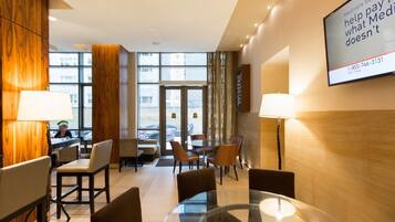 A hotel lobby with a glass table, chairs, a reception desk, and a large screen displaying Medicare information.