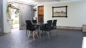 Een terras buiten met een tafel, stoelen, een plafondventilator en een lijst met een afbeelding aan de muur.