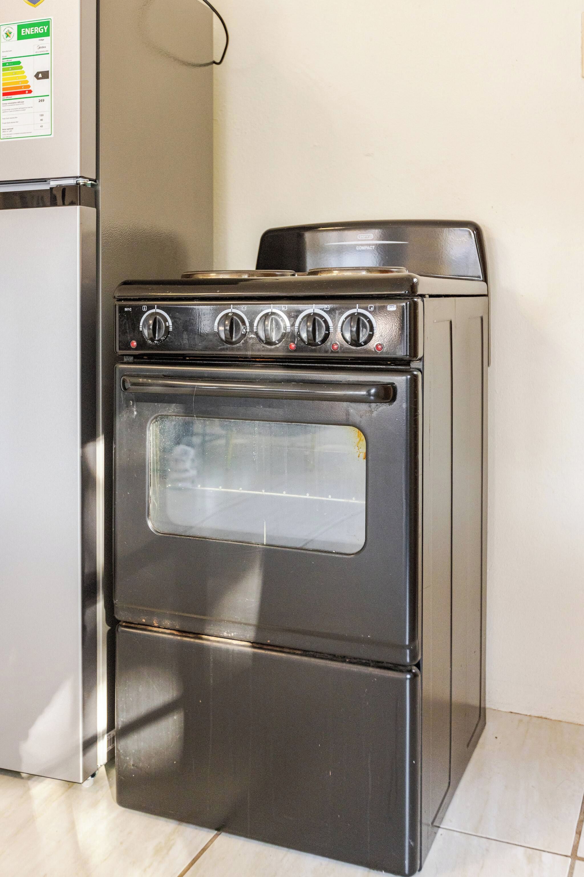 Een compacte oven van roestvrij staal met vier knoppen en één deur, in een keuken met een witte koelkast links ervan.