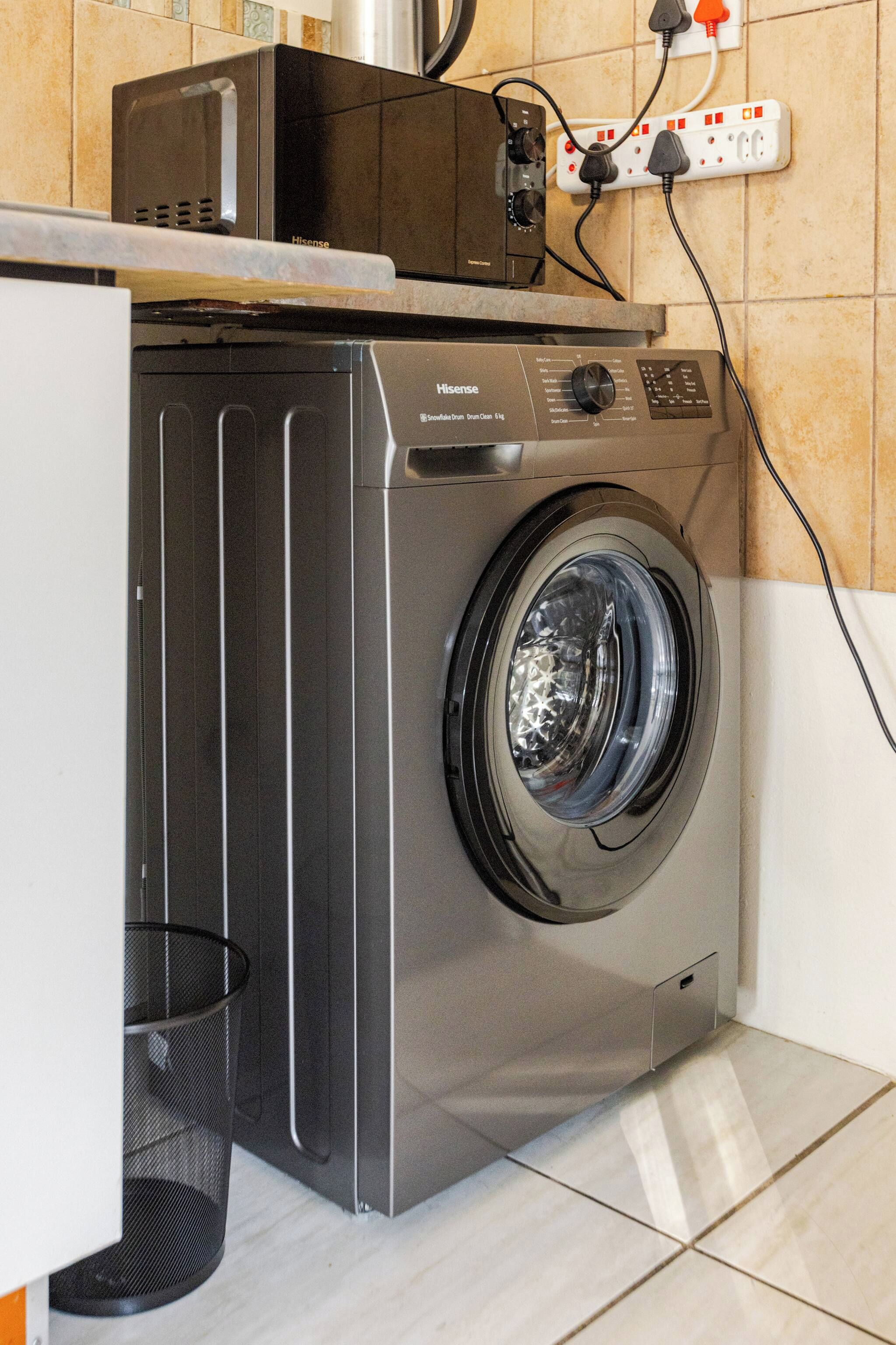 Een wasmachine met een voorlaadopening, een bedieningspaneel, een stopcontact en een prullenbak in een keuken.