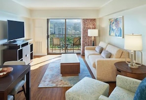 Una sala de estar moderna con un sofá, sillones, una mesa de centro y un televisor sobre un mueble. Hay un balcón con vistas a la ciudad.