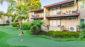 Un edificio residenziale con un balcone, un piccolo patio e un prato curato con una buca da golf.