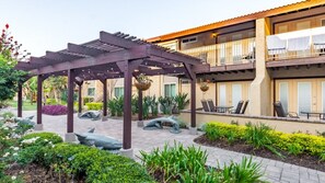 Ein überdachter Außenbereich mit einer Pergola, Sitzgelegenheiten und einer Liege am Pool.