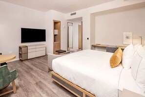 Quarto de hotel moderno com uma cama grande, TV de tela plana, escrivaninha e área de estar.