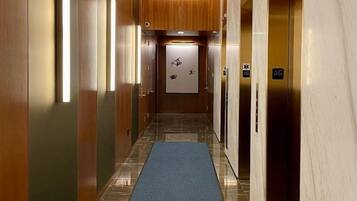 A modern hotel corridor with wooden paneling, marble floors, and blue carpeting.