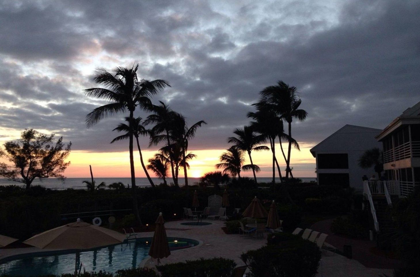 A resort with a pool, palm trees, and a view of the sunset.