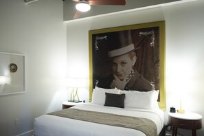 Una habitación de hotel con una cama grande, una mesita de noche, una lámpara y un cuadro colgado en la pared.