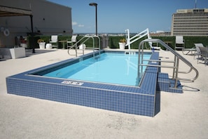 Ein Pool auf dem Dach mit Blick auf die Stadtlandschaft, umgeben von Liegestühlen und einem Rettungsschwimmerstand.