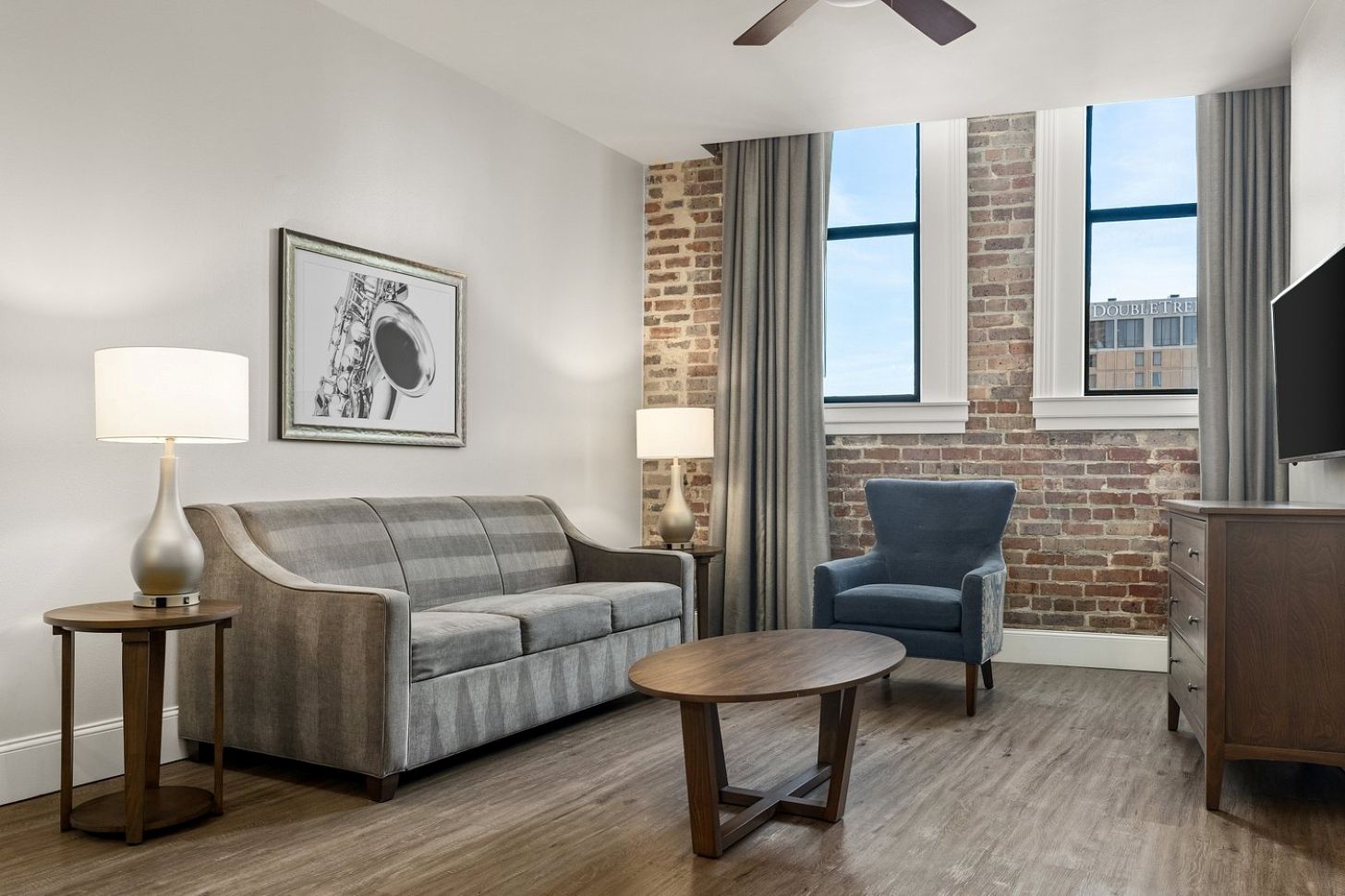 A modern living room with a grey sofa, a blue armchair, a round wooden coffee table, and two floor lamps.
