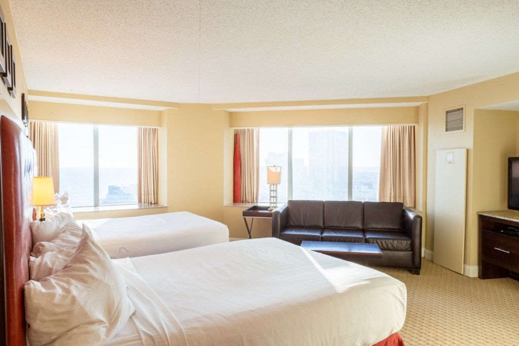 A hotel room with two beds, a sofa, a TV, and large windows with curtains.